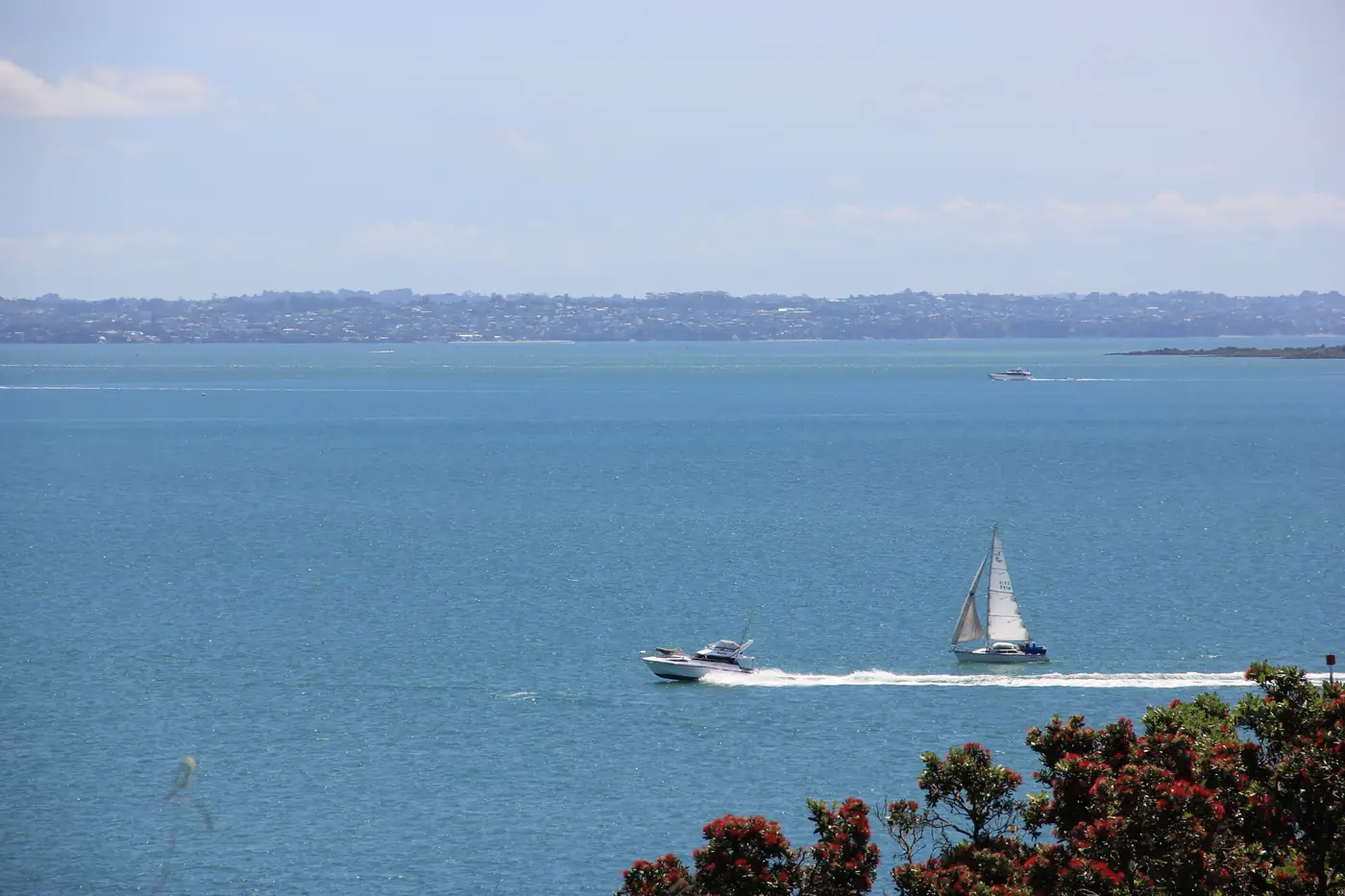 A launch and a sailboat crossing calm blue water on a clear day