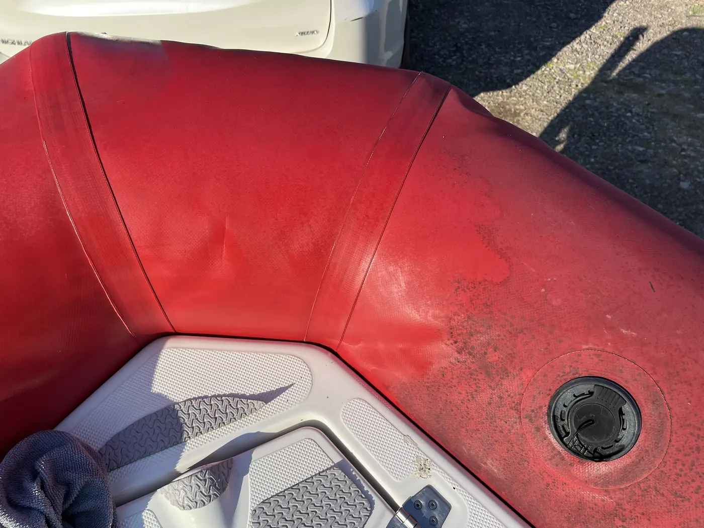 A red inflatable boat tube partway through cleaning: the left side is clean and glossy, the right side is still dull and spotted with mould